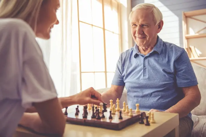 old man playing chess with caregiver